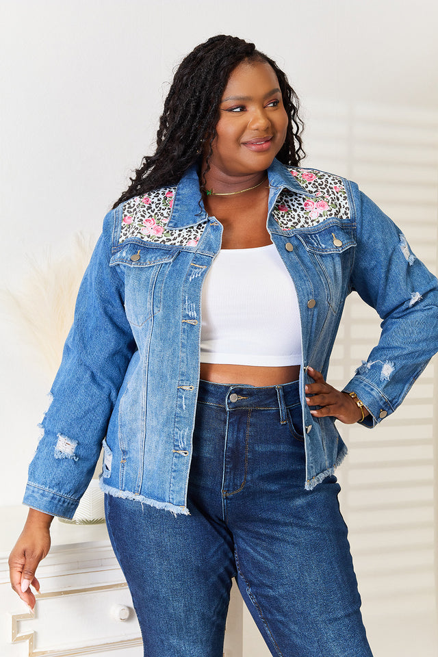 Woman wearing a denim jacket with floral embellishments and jeans, standing against a white background.