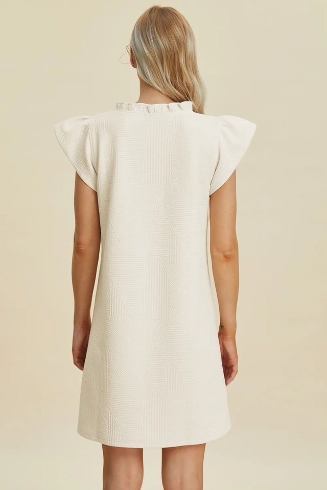 Woman wearing a white dress with ruffled sleeves on a beige background