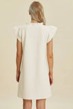 Woman wearing a white dress with ruffled sleeves on a beige background