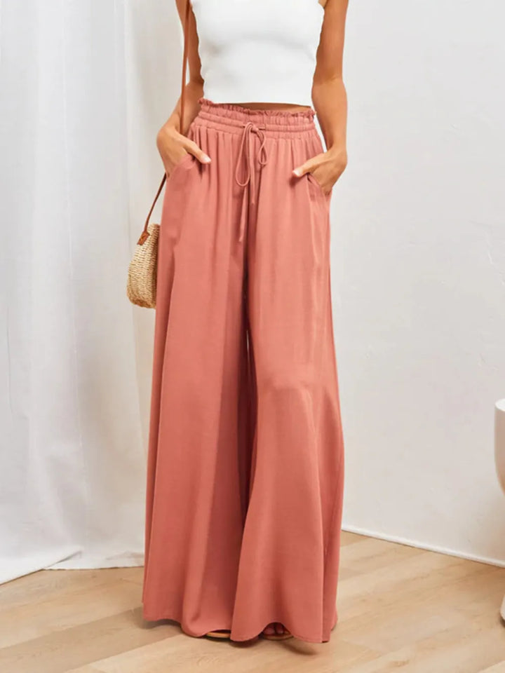 Person wearing pink wide-leg pants and a white top, standing against a plain background.