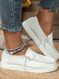 White sneakers worn with denim jeans on a woven surface.