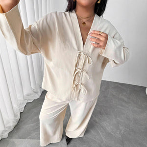 Person wearing a beige outfit standing in a minimalistic room with white curtains.
