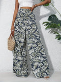 Person wearing tropical leaf print pants with a white top and sandals, holding a woven bag.