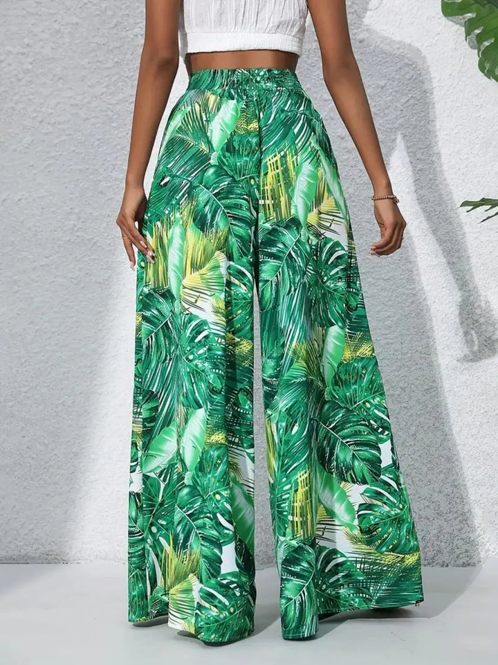 Green tropical leaf patterned pants worn by a person on a light gray background