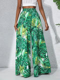 Green tropical leaf patterned pants worn by a person on a light gray background