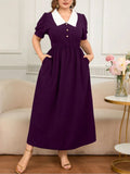 Woman wearing a purple dress with a white collar in a living room setting.