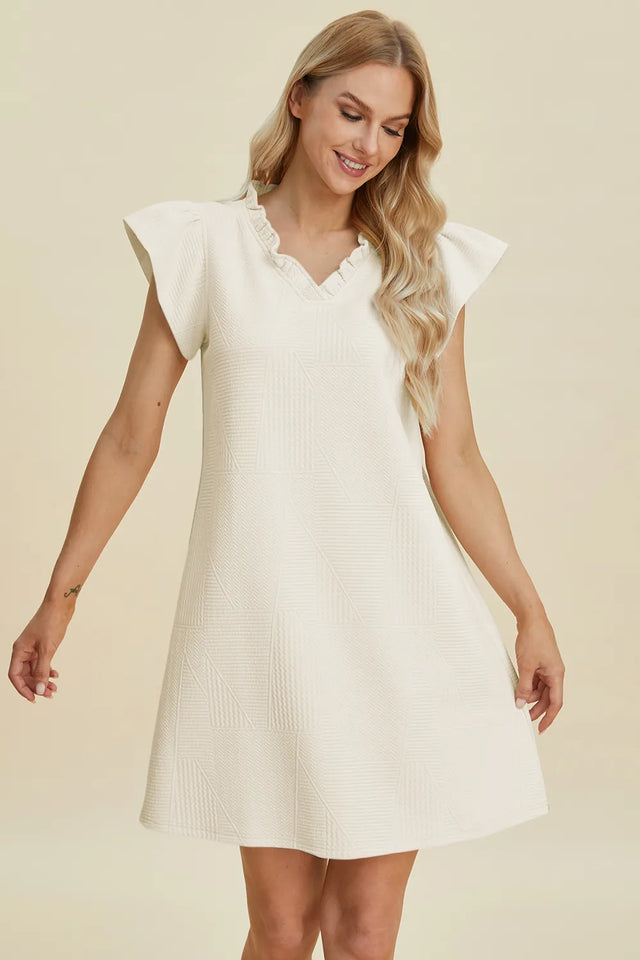 Woman wearing a white dress with ruffled sleeves on a beige background
