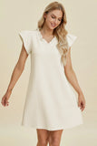 Woman wearing a white dress with ruffled sleeves on a beige background