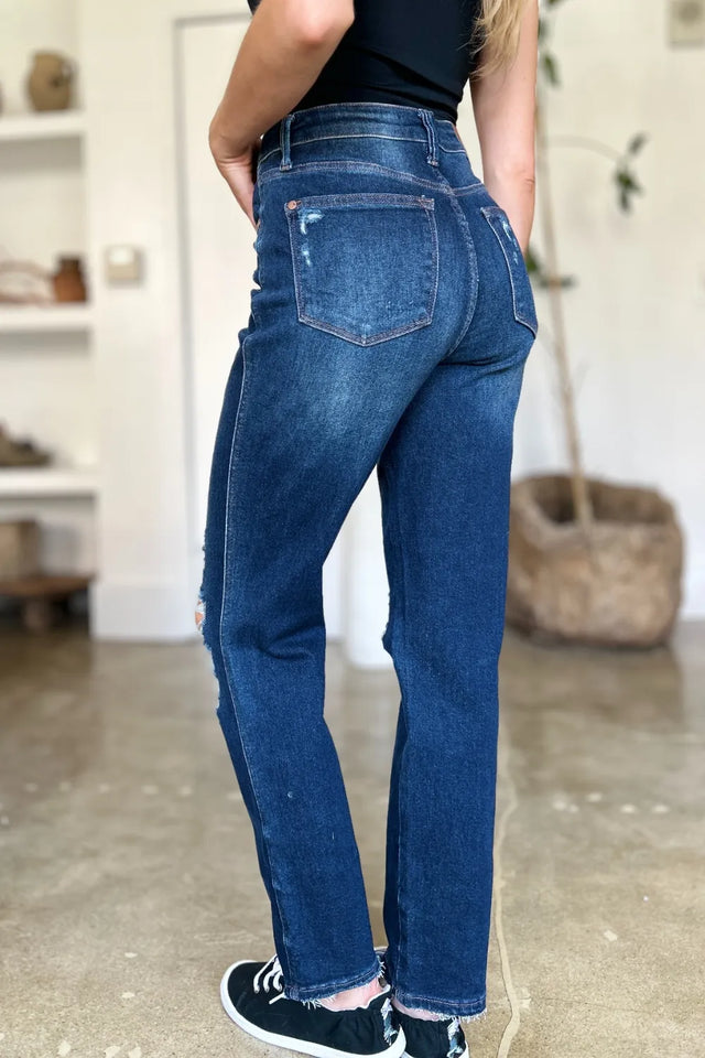 Person wearing blue jeans standing in a room with a neutral background