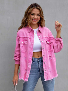 Woman wearing a pink denim jacket over a white top and blue jeans against a gray background