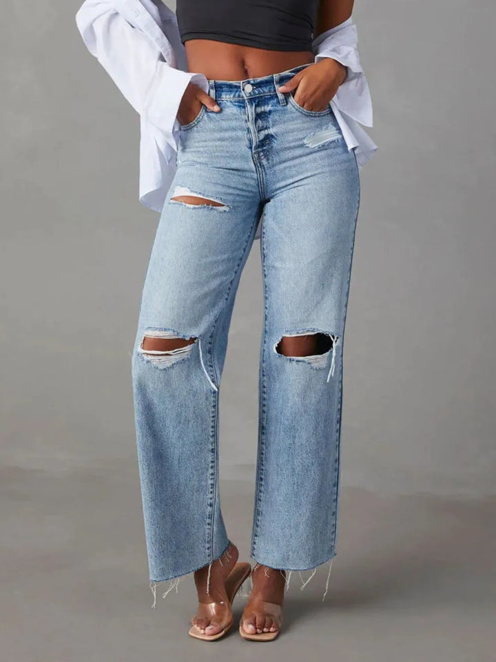 Ripped blue jeans worn by a person on a gray background