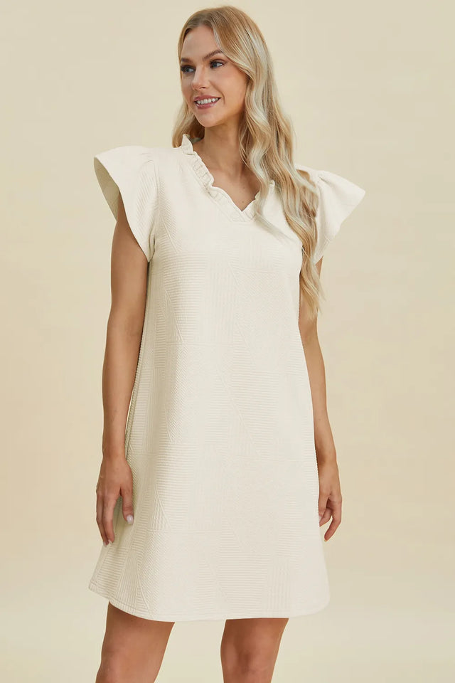 Woman wearing a white dress with ruffled sleeves on a beige background