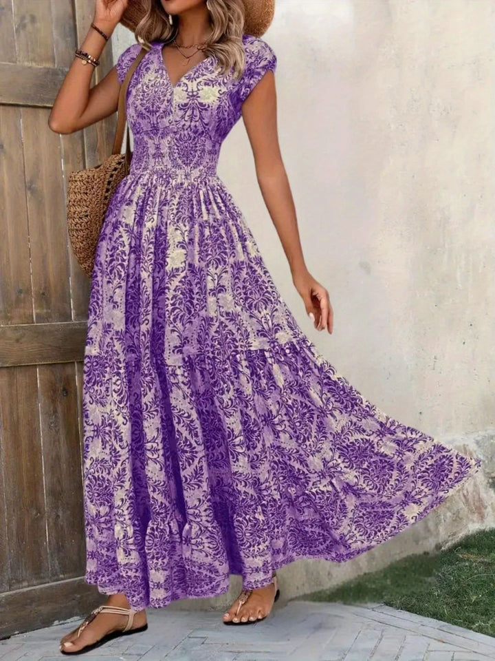 Woman wearing a purple floral dress standing against a wooden wall.
