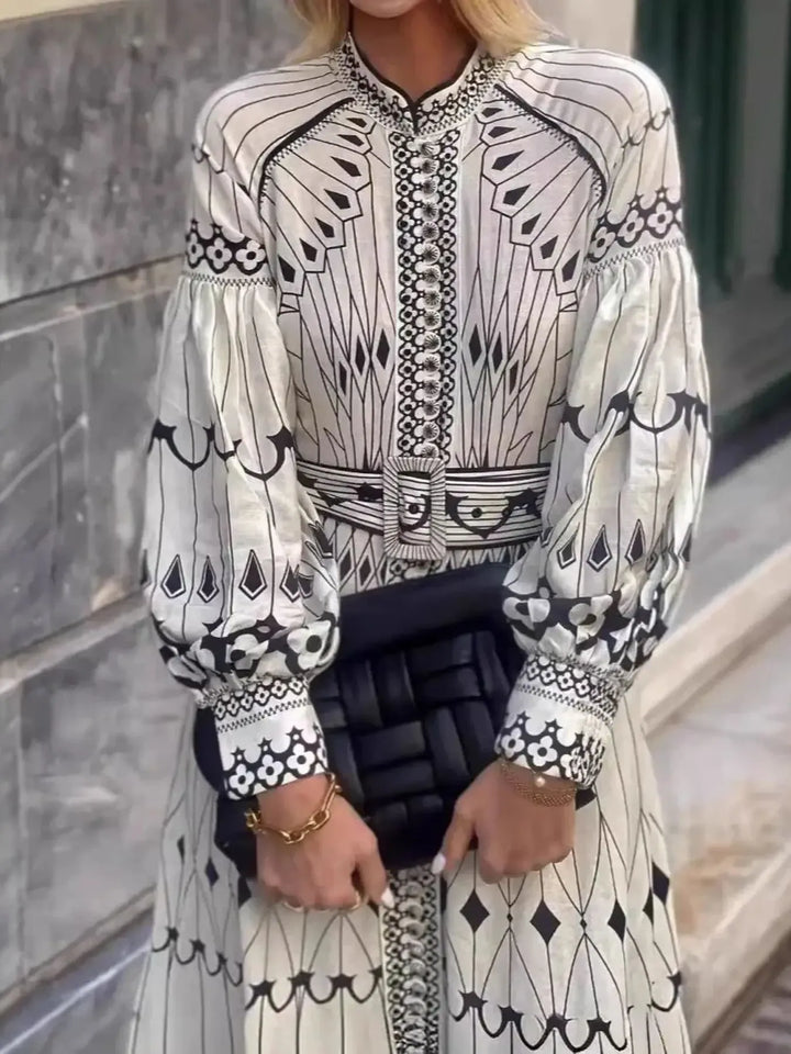 Person wearing a black and white patterned outfit with long sleeves, standing against a stone wall.