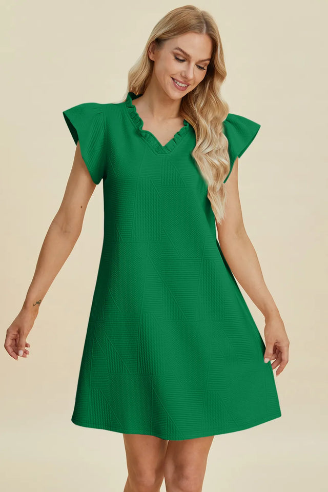 Woman wearing a green dress with ruffled sleeves on a beige background