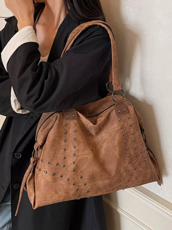 Brown suede handbag with studs held by a person against a neutral background