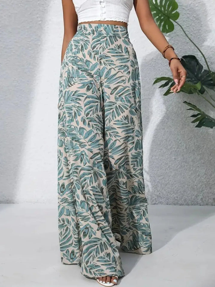Person wearing tropical leaf-patterned pants with a white top against a gray background