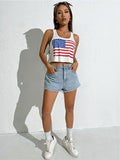Person wearing an American flag tank top and denim shorts against a white wall.