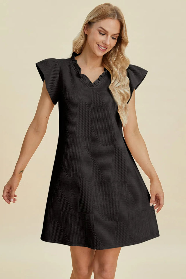Woman wearing a black dress with ruffled sleeves on a beige background