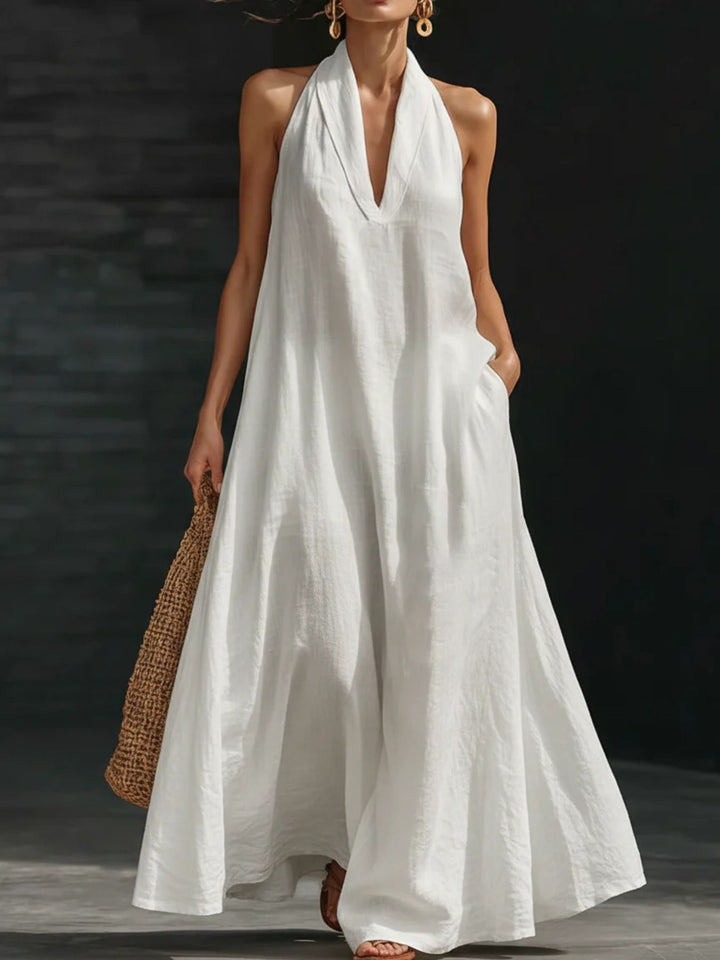Woman wearing a white halter neck dress holding a woven bag against a dark background
