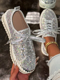 Silver glittery sneakers with rhinestone laces held by a hand against a blurred background.