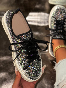 Glittery sneaker with black laces held by a hand against a blurred background