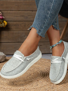 Gray loafers worn with denim jeans on a wooden floor.