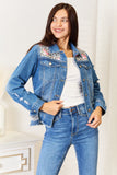 Woman wearing a blue denim jacket with floral embroidery and matching jeans indoors.