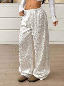 Person wearing white leopard print pants in a room with a wooden floor and light-colored walls.