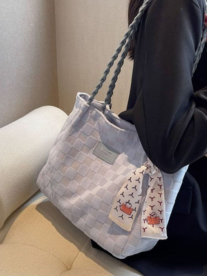 Person holding a woven handbag with a matching pouch on a beige couch
