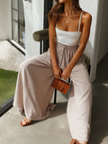 Woman sitting outdoors wearing a white top and beige wide-leg pants, holding a brown leather clutch.