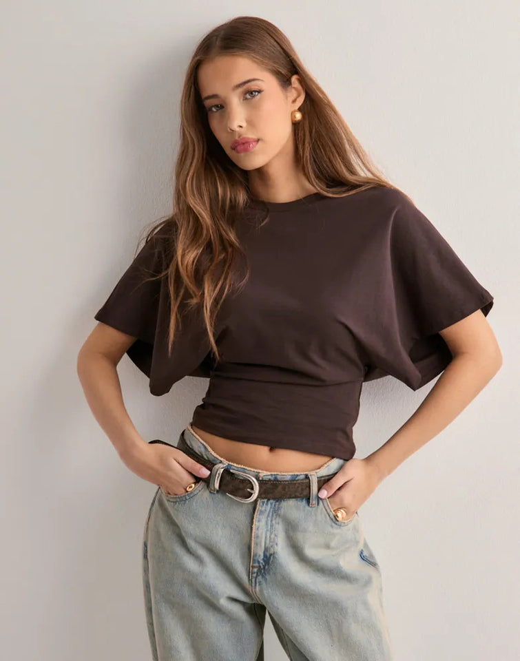 Woman wearing a brown top and light blue jeans against a plain background