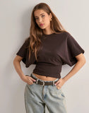 Woman wearing a brown top and light blue jeans against a plain background