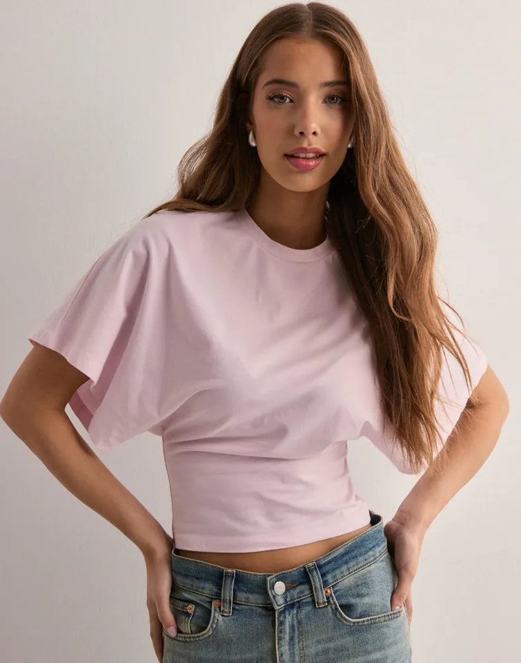 Woman wearing a light pink crop top and blue jeans against a plain background