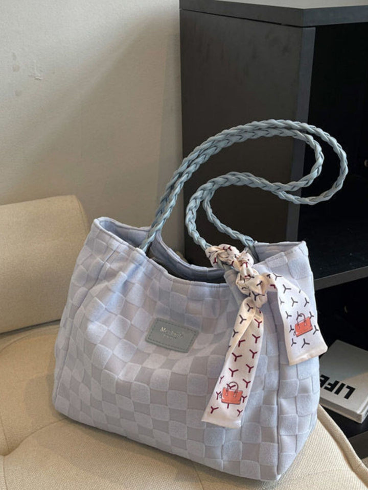 Gray checkered handbag with a decorative ribbon on a beige surface