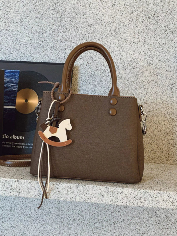 Brown handbag with a rocking horse charm on a textured surface