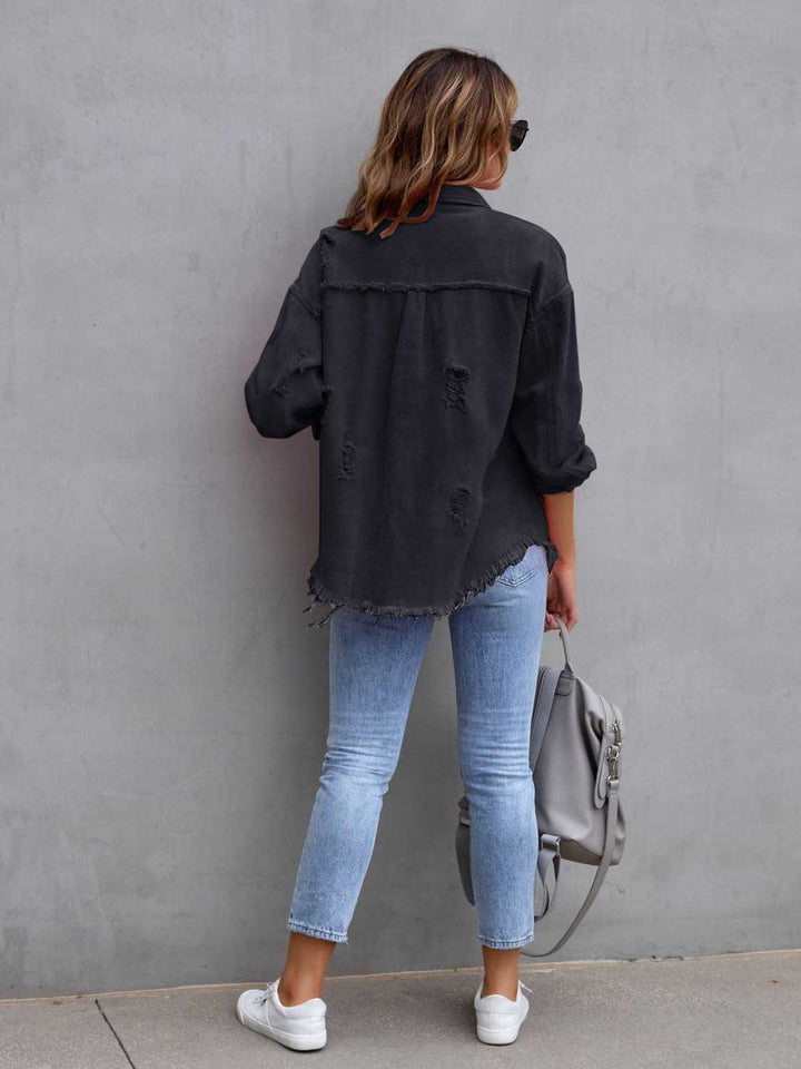 Person wearing a black jacket and light blue jeans against a gray wall