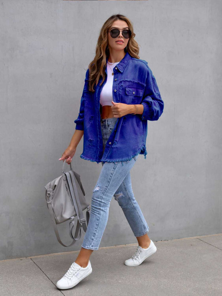 Woman wearing a blue denim jacket, white sneakers, and light blue jeans against a gray wall.
