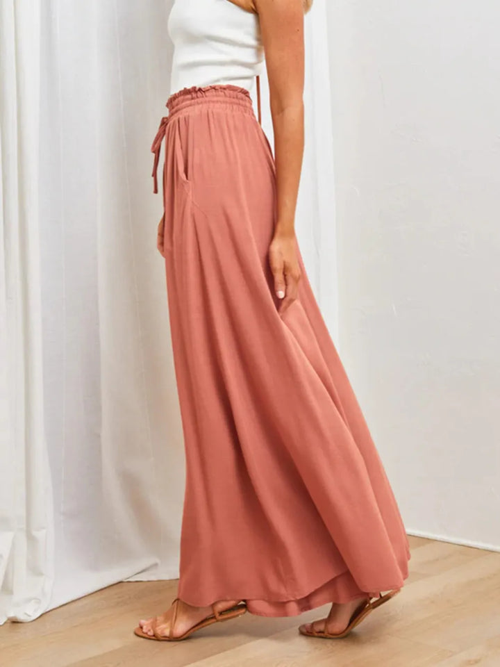 Person wearing a pair of wide-leg pants with a white top and sandals on a light wooden floor.