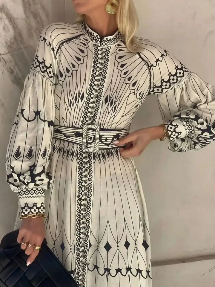 Woman wearing a long, patterned dress with a belt against a neutral background