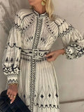 Woman wearing a long, patterned dress with a belt against a neutral background