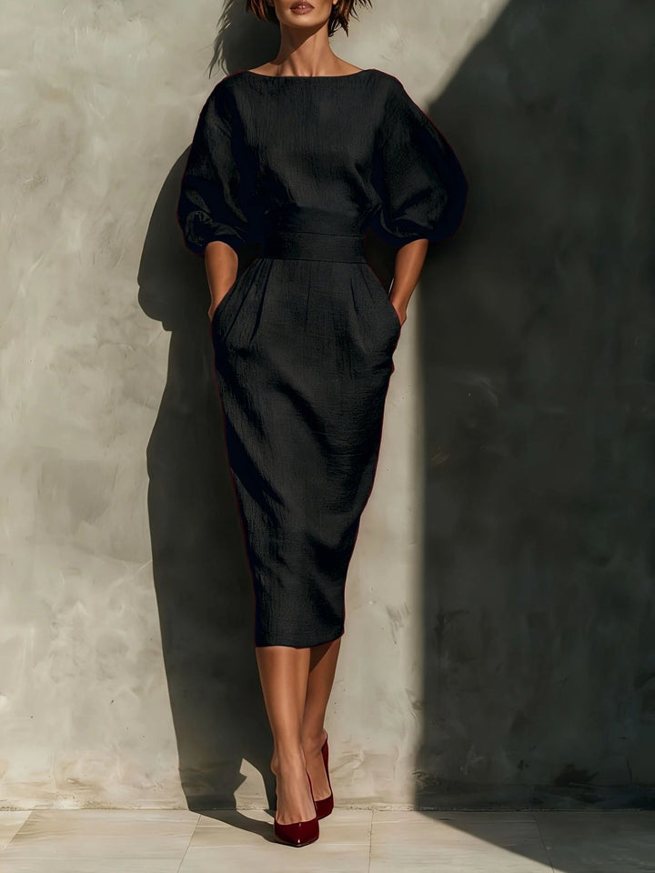 Woman wearing a black dress against a textured wall.