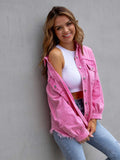 Woman wearing a pink denim jacket over a white top and blue jeans against a gray wall.