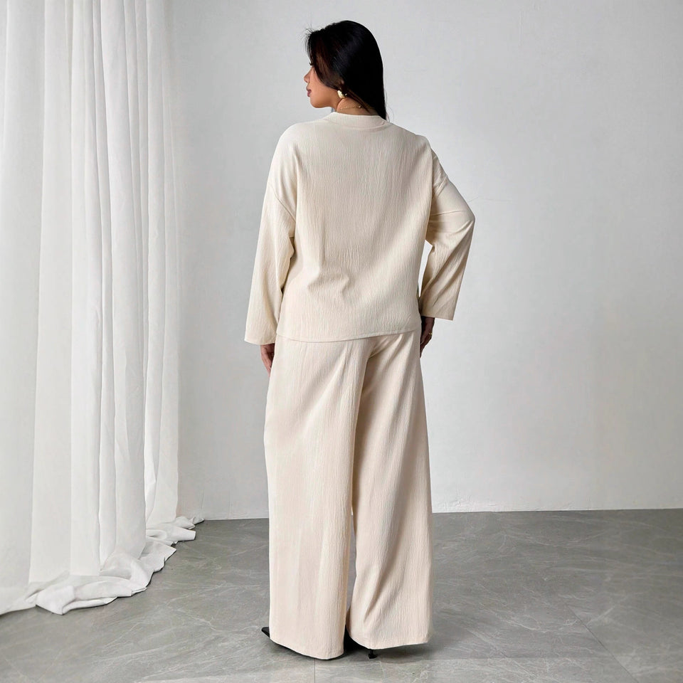 Person wearing a beige outfit standing in a minimalistic room with white curtains.