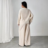 Person wearing a beige outfit standing in a minimalistic room with white curtains.