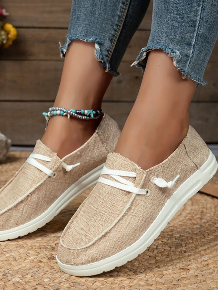 Beige loafers with white soles worn by a person on a wooden floor.