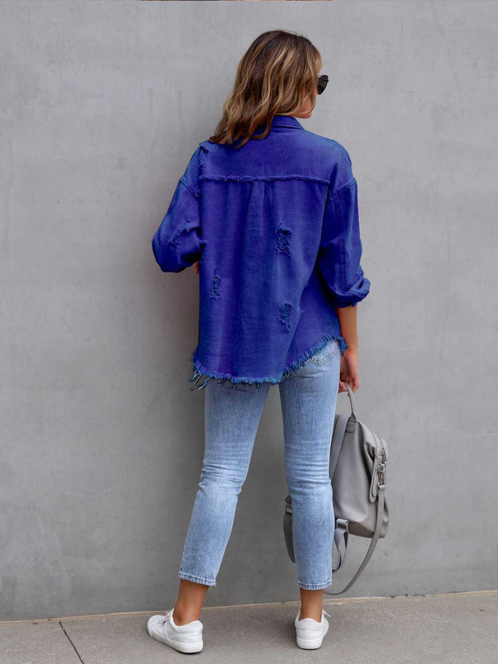 Person wearing a blue denim jacket and light blue jeans against a gray wall.