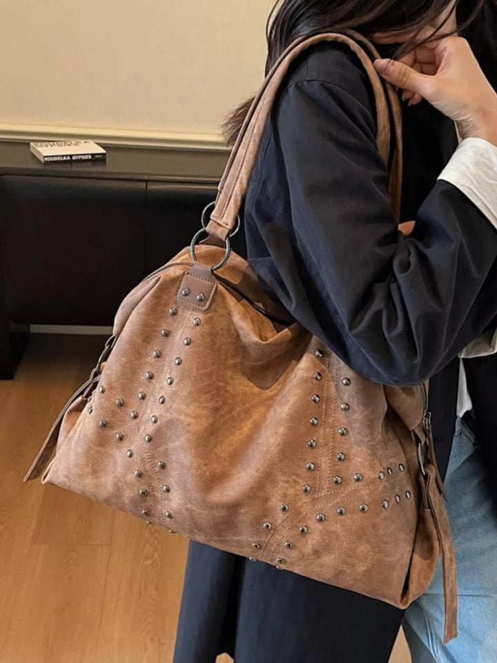 Person holding a brown suede handbag with studs indoors