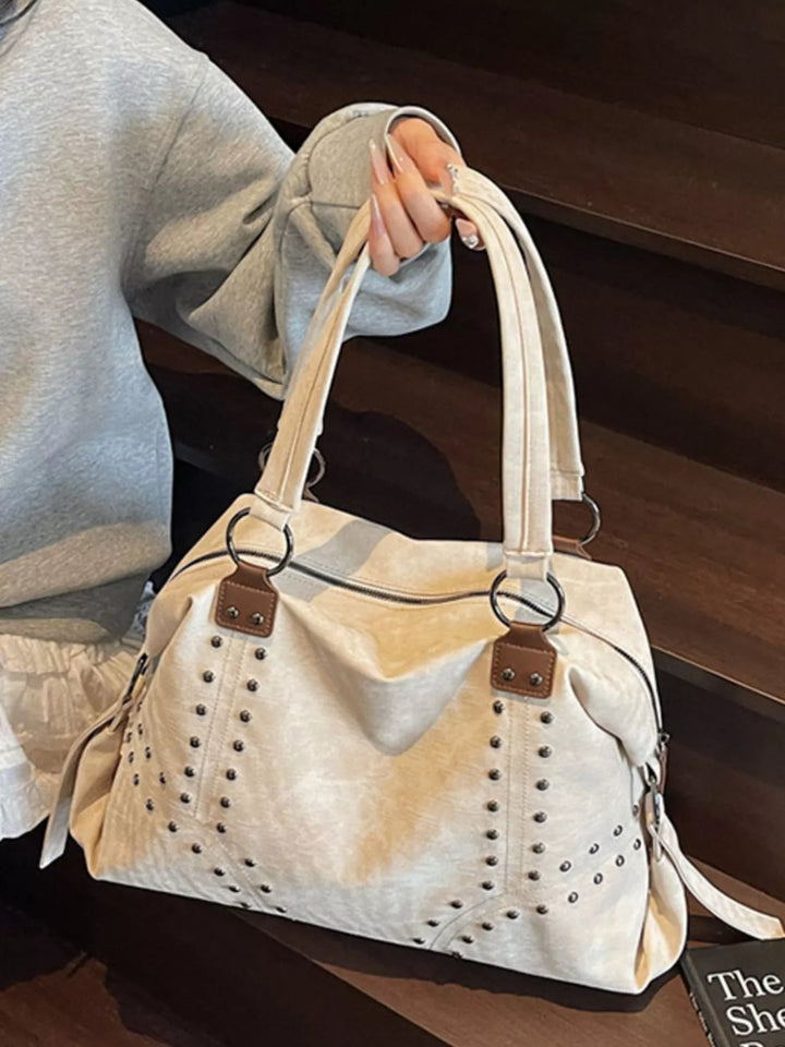 Beige handbag with brown accents held by a person wearing a light gray sweatshirt.