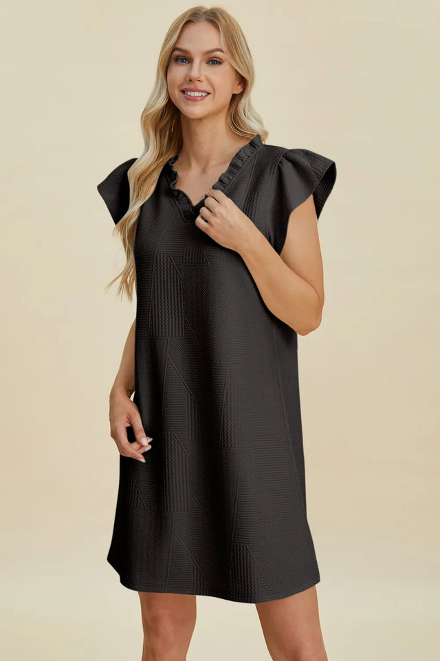 Woman wearing a black dress with ruffled shoulders on a beige background